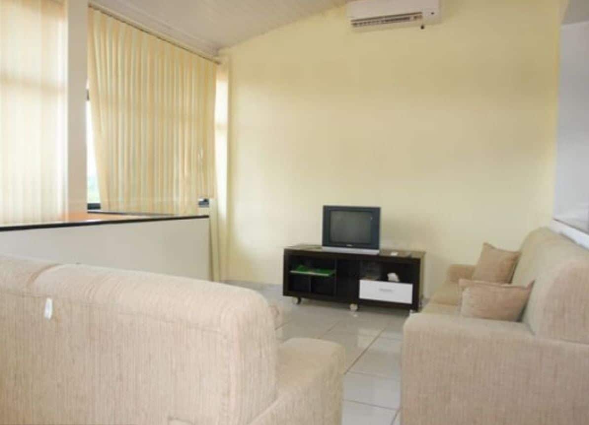 A living room with beige sofas, a television on a black stand, and a window with vertical blinds.