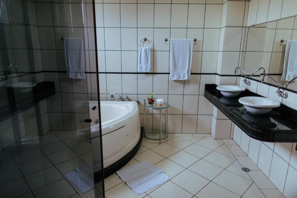 Een moderne badkamer met een douche met glazen wand, een badkuip en twee wastafels met zwarte aanstootplaten.