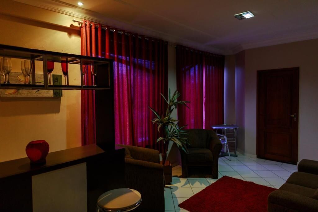 Een woonkamer met een rood gordijn, een plant, een trommel en een bank.
