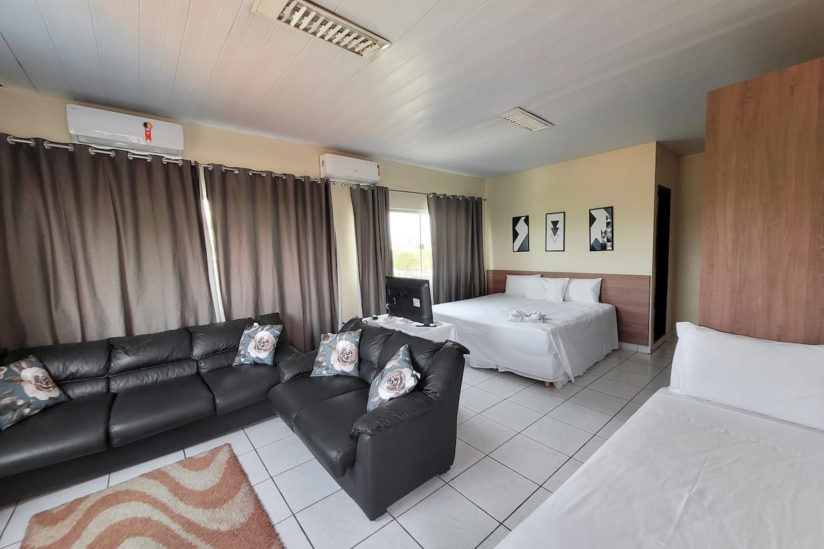 A hotel room with a black leather sofa, a bed, a desk with a computer, and a window with curtains.