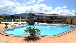 A swimming pool with lounge chairs and a covered area, surrounded by greenery and mountains. - Carajas Hotel (Parauapebas)