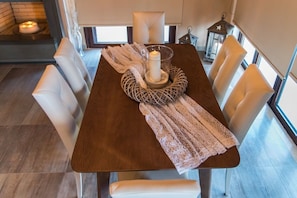 Una mesa de comedor con un centro de velas, sillas blancas y un mantel tejido.