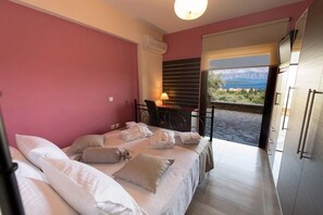 A bedroom with a bed, pillows, a desk with a lamp, and a view of a mountainous landscape through a window. - Luxurious Villa Kastro (Lefkada)