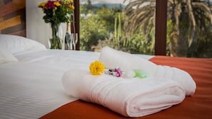 A neatly made bed with a folded towel, a yellow flower, and a bottle of lotion on the bed. - Ilalo Garden Hotel & Restaurant (Tumbaco)