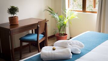 Une chambre d’hôtel bien rangée, avec un lit, une serviette bleue, une petite plante en pot, un bureau en bois et une chaise.