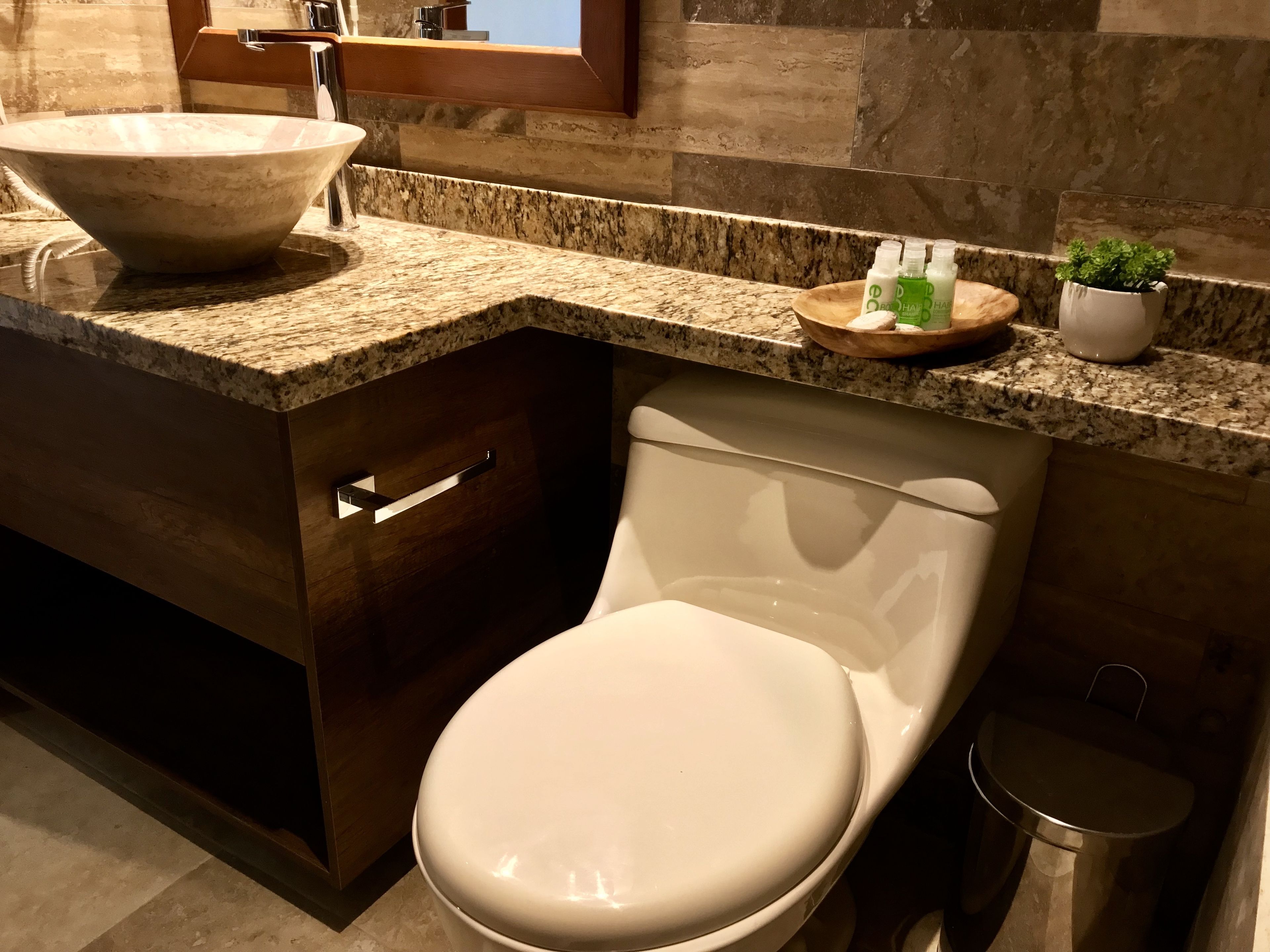 A modern bathroom with a large vessel sink, a toilet, and a small trash can.