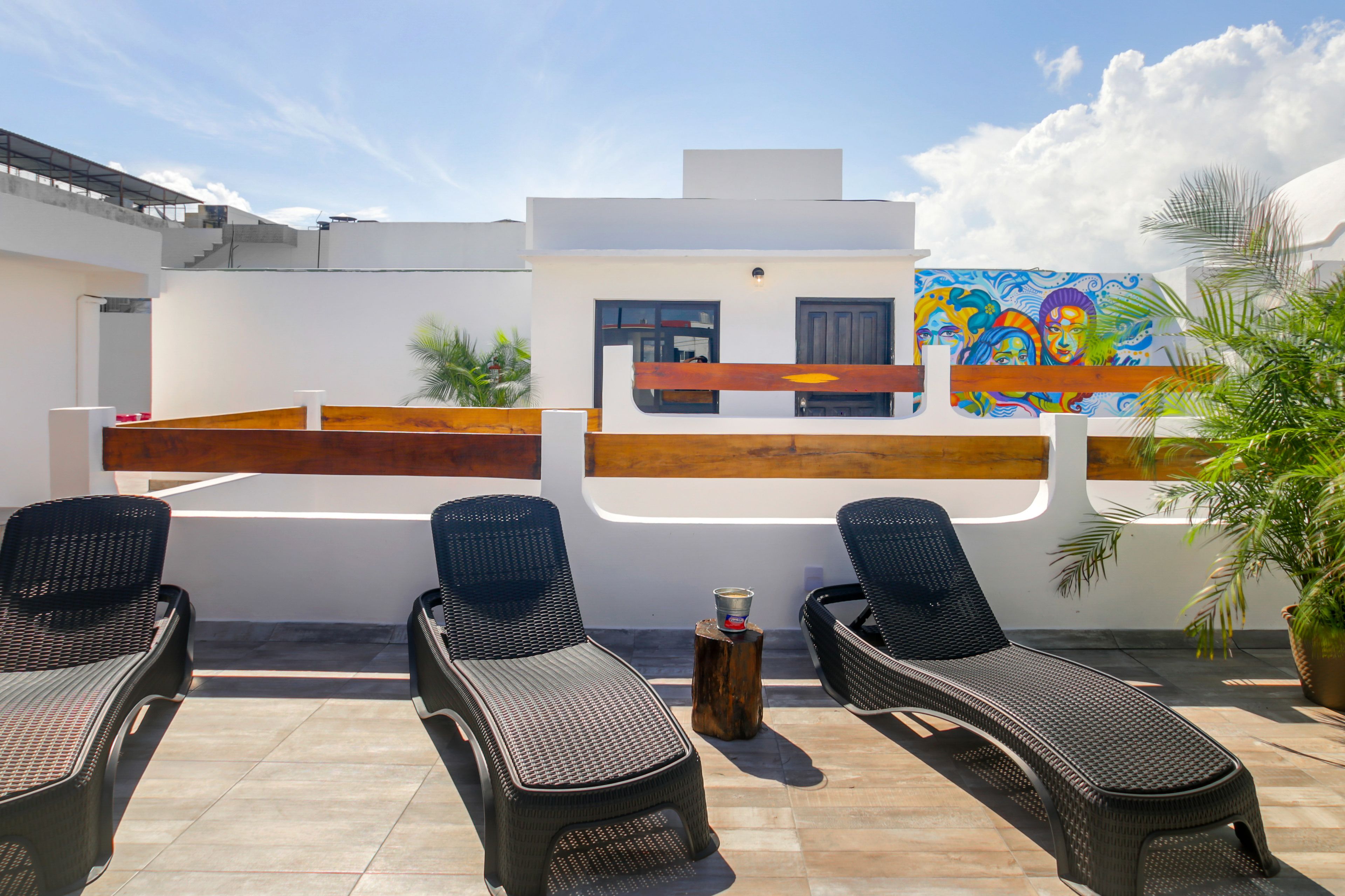 Un área de lounge en la azotea con tres sillones, un banco de madera y un mural colorido en la pared.