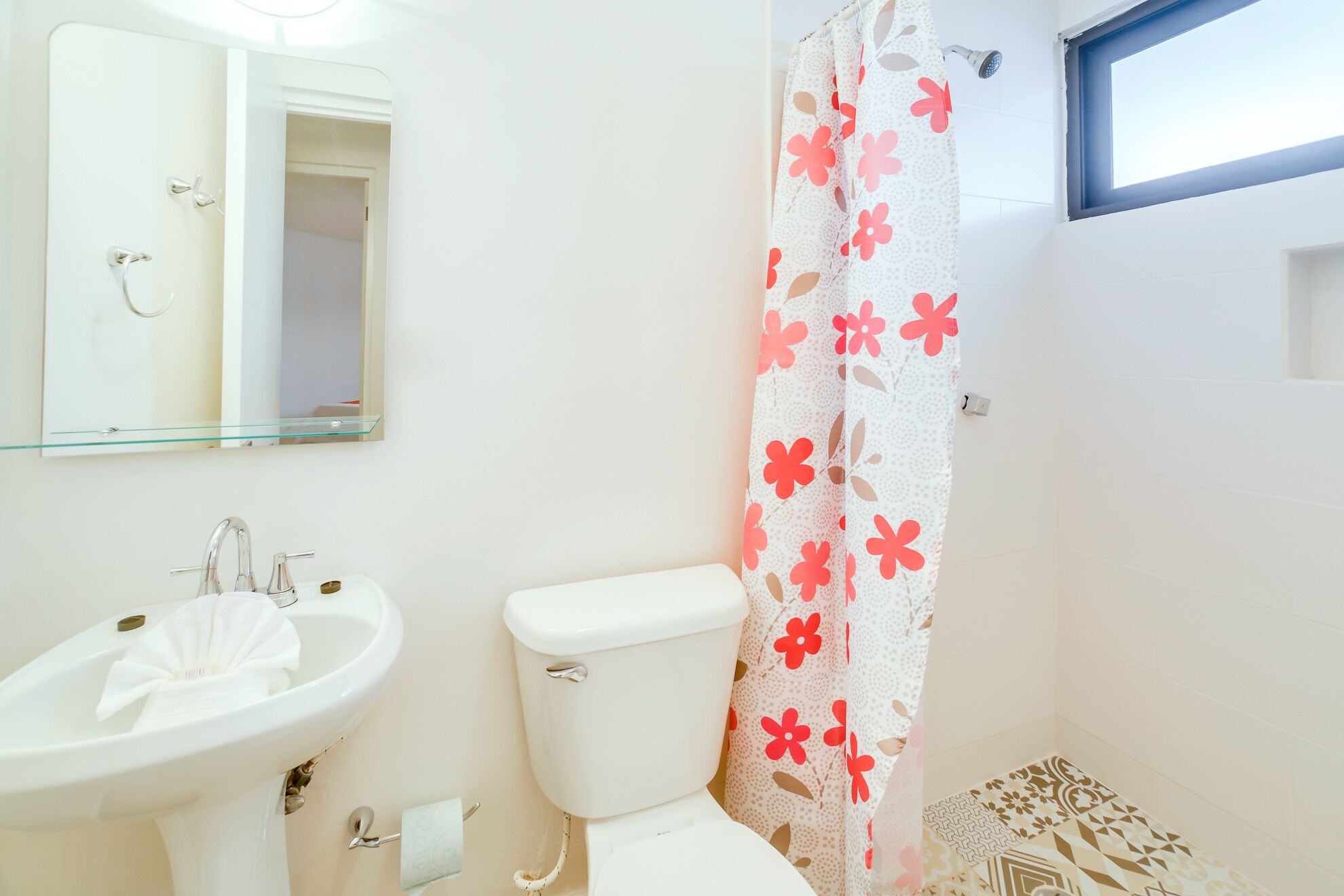 A bathroom with a white sink, a toilet, a shower curtain with a floral pattern, and a mirror above the sink.