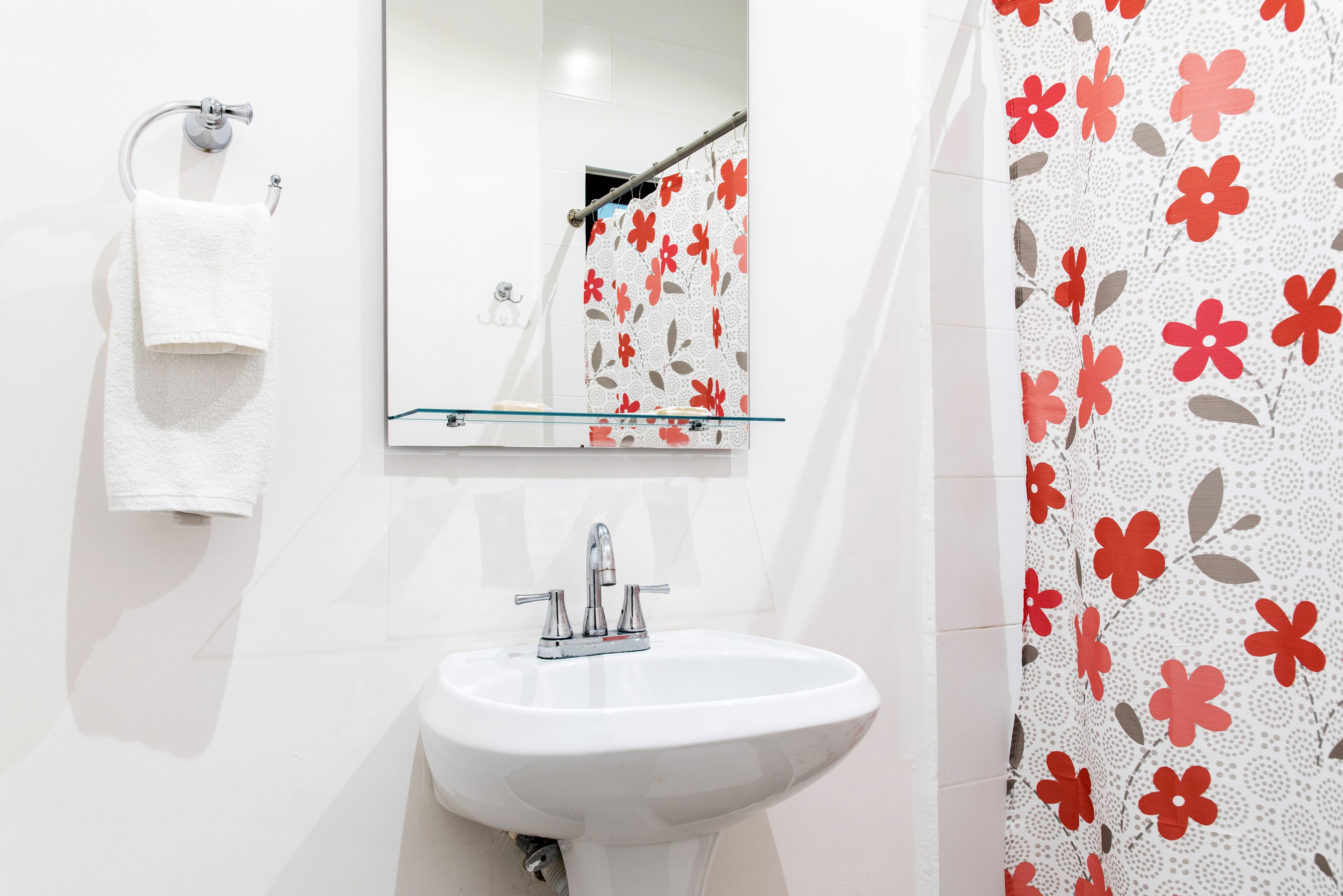 Casa de banho com lavatório branco, espelho e porta-toalhas.