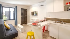 A modern kitchen with a central island, white cabinetry, and a dining area with a sofa and yellow stool. - Valentina Suites by Las Flores (Playa del Carmen)