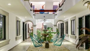 A spacious, well-lit hallway with a central seating area featuring modern chairs, a decorative fountain, and potted plants. - Valentina Suites by Las Flores (Playa del Carmen)