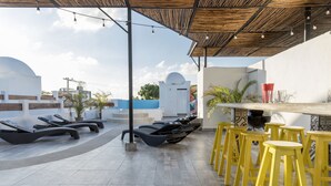 A rooftop terrace with lounge chairs and yellow stools, a bar area, and a view of the cityscape. - Valentina Suites by Las Flores (Playa del Carmen)