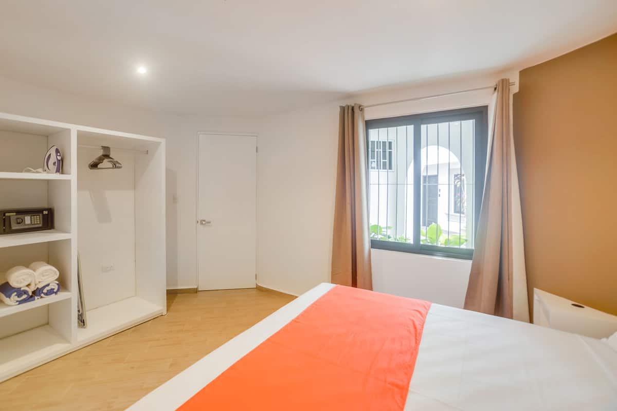 A hotel room with a bed, a wardrobe, a window with curtains, and a view of the outside.