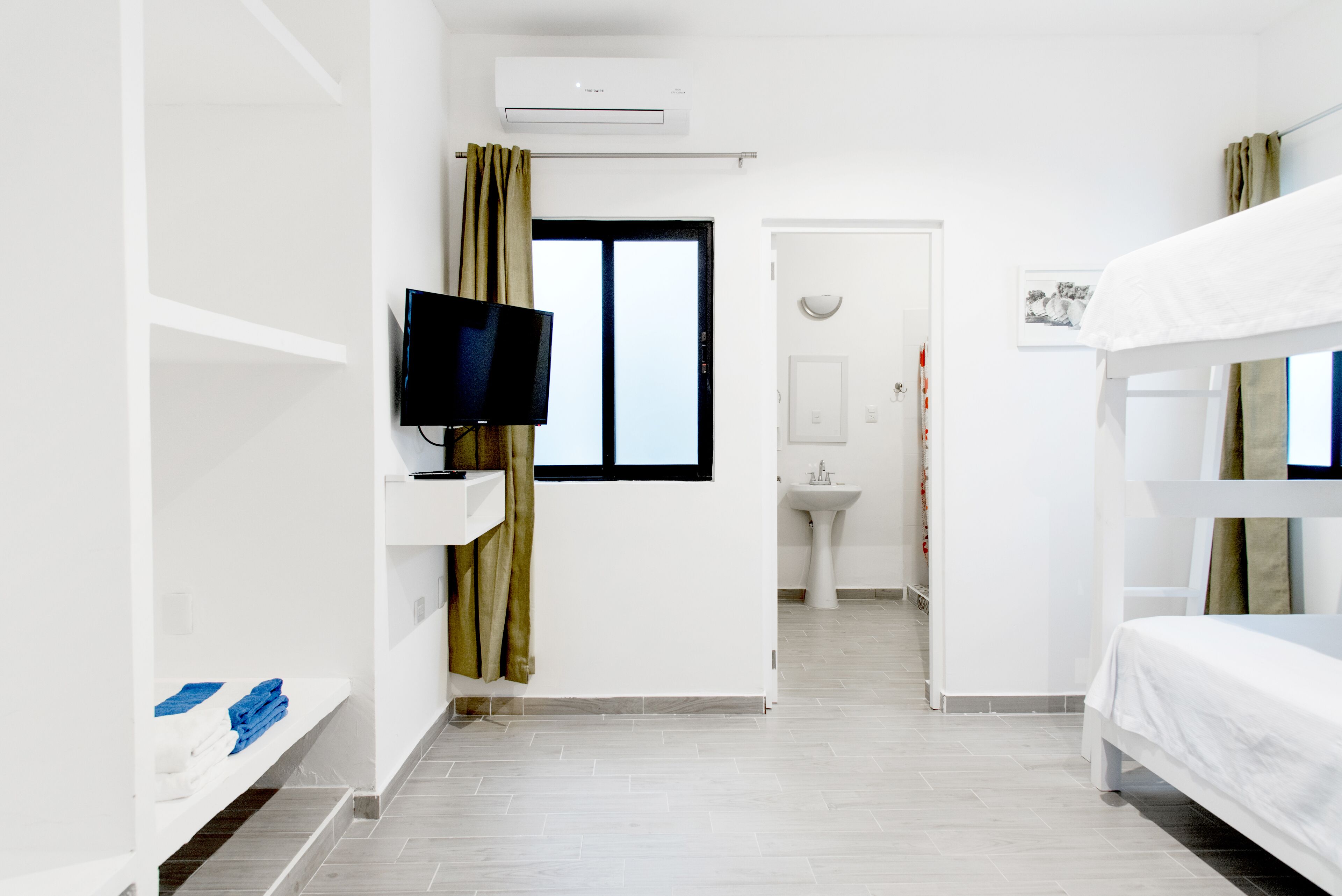 A hotel room with a television, a sink, a window with curtains, and a bunk bed.