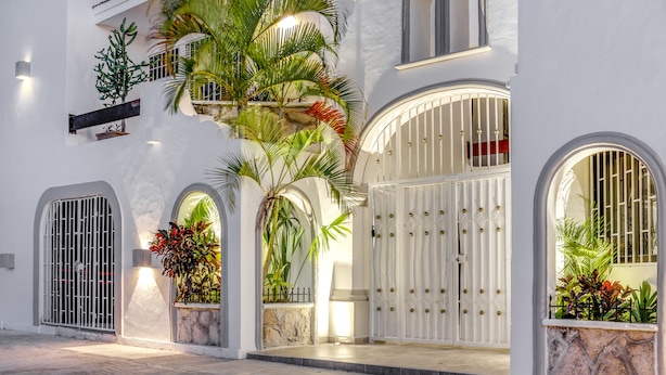 A white building with arched doorways, a gated entrance, and potted plants. - Valentina Suites by Las Flores (Playa del Carmen)