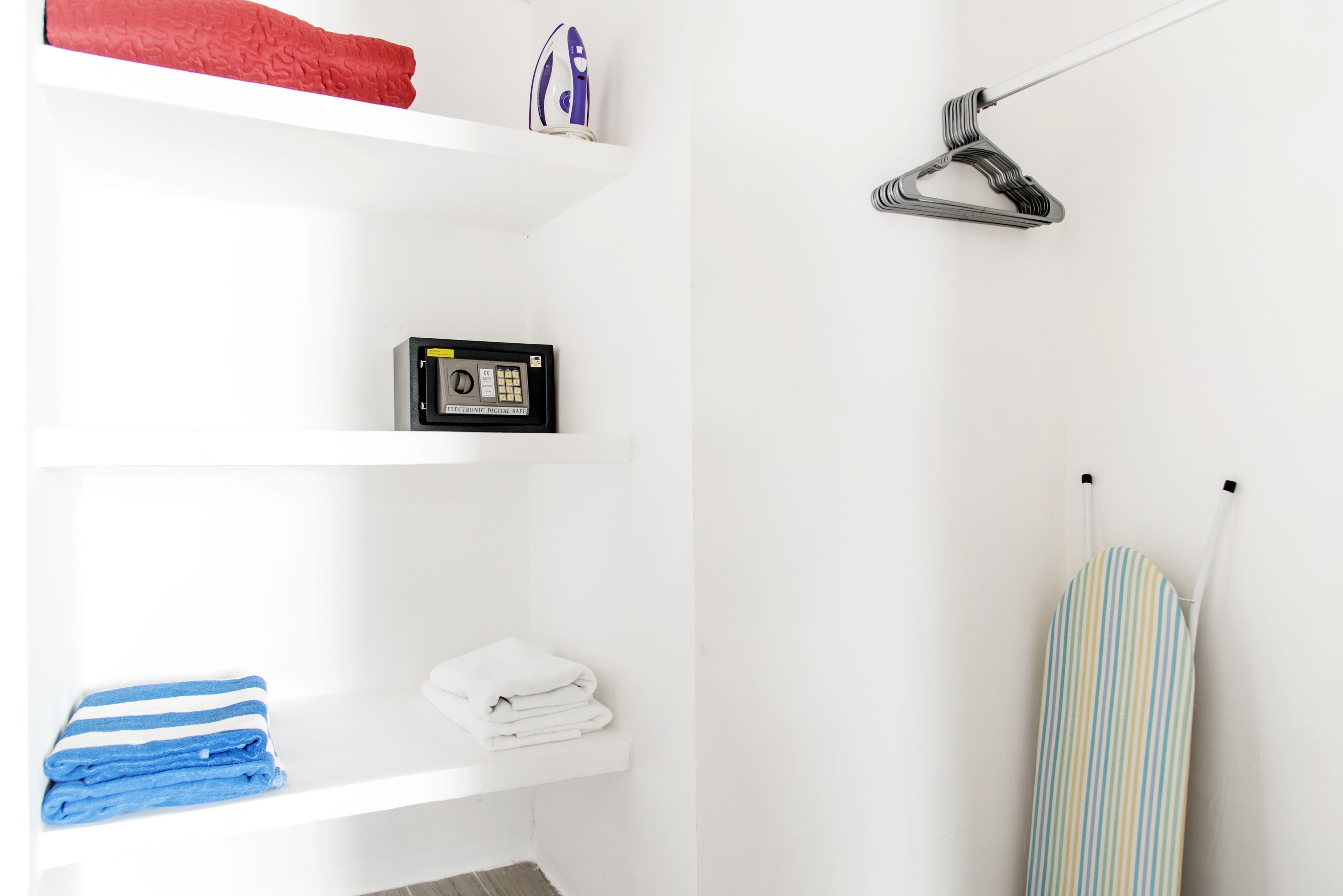 A neatly organized bathroom with a white shelf holding a red towel, a blue towel, and a white towel. There is a black radio on another shelf. A white hanging shower curtain rod with a striped shower curtain is also visible.