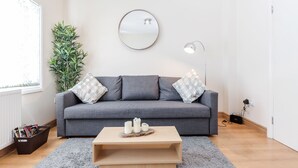A modern living room with a grey sofa, a round mirror, and a wooden coffee table. - Lovely Apartment Angel (London)