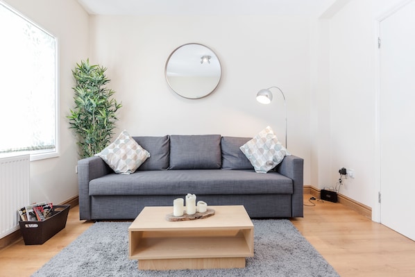 A modern living room with a grey sofa, a round mirror, and a wooden coffee table.