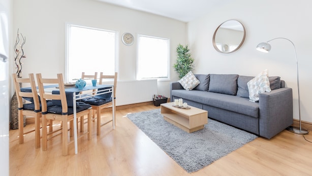 A modern living room with a grey sofa, wooden chairs, a coffee table, and a large window. - Lovely Apartment Angel (London)