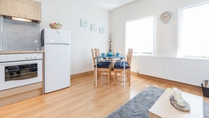A modern kitchen with a built-in oven, a white refrigerator, and a dining area with a table and chairs. - Lovely Apartment Angel (London)
