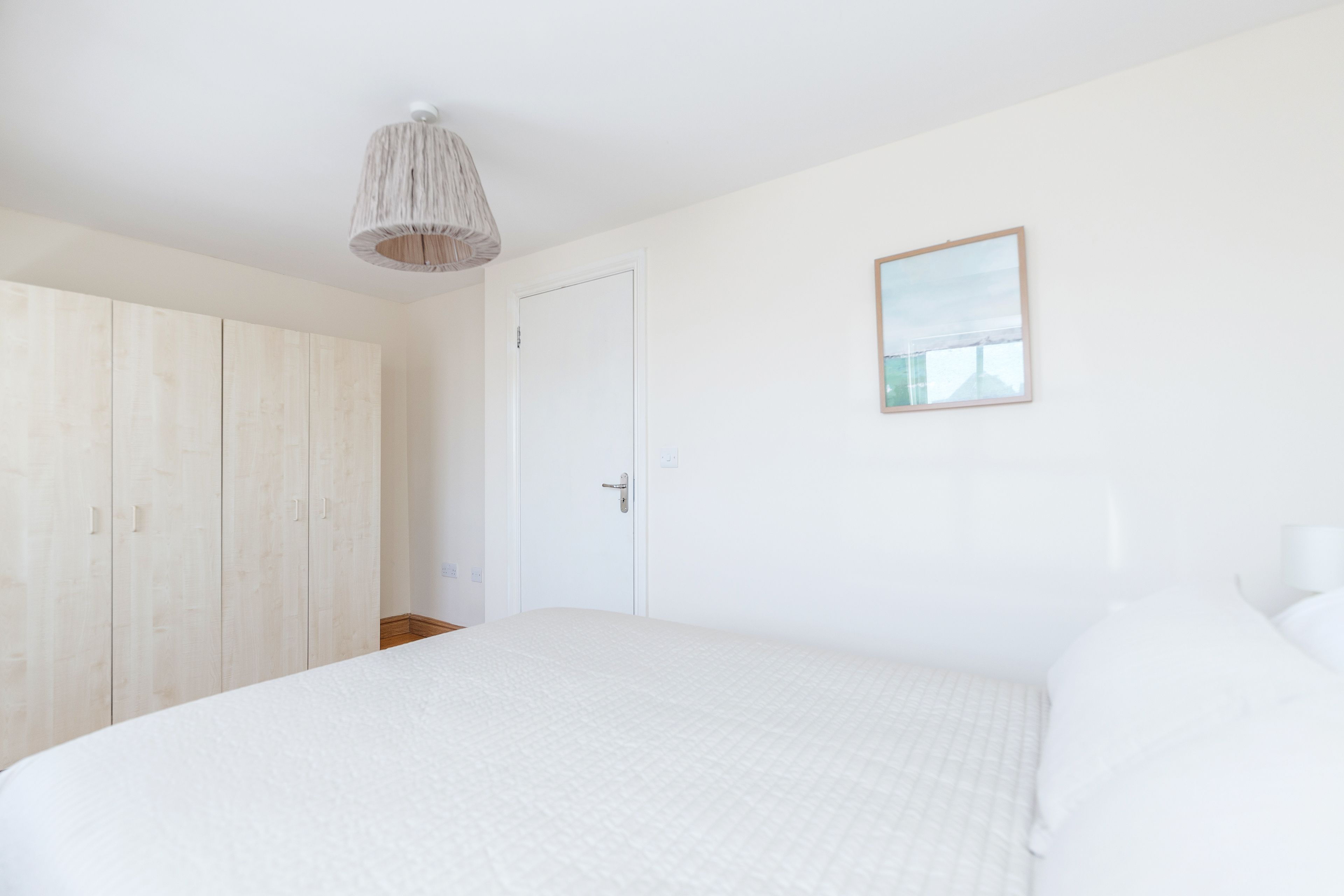 Une chambre à coucher avec un grand lit, une armoire, une porte et un tableau encadré au mur.