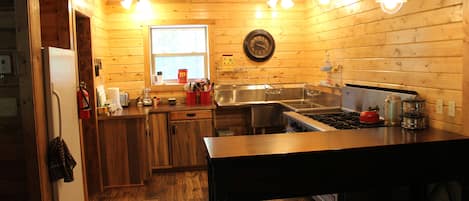 A wooden cabin kitchen with a refrigerator, sink, stove, and wooden cabinets.