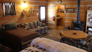 A cozy log cabin room with a bed, sofa, and a small dining table. - Sugar Loaf Lodge & Cabins (Anaconda)