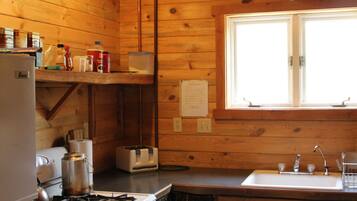 A compact kitchen with wooden walls, a gas stove, a refrigerator, a sink, and a window with a view.