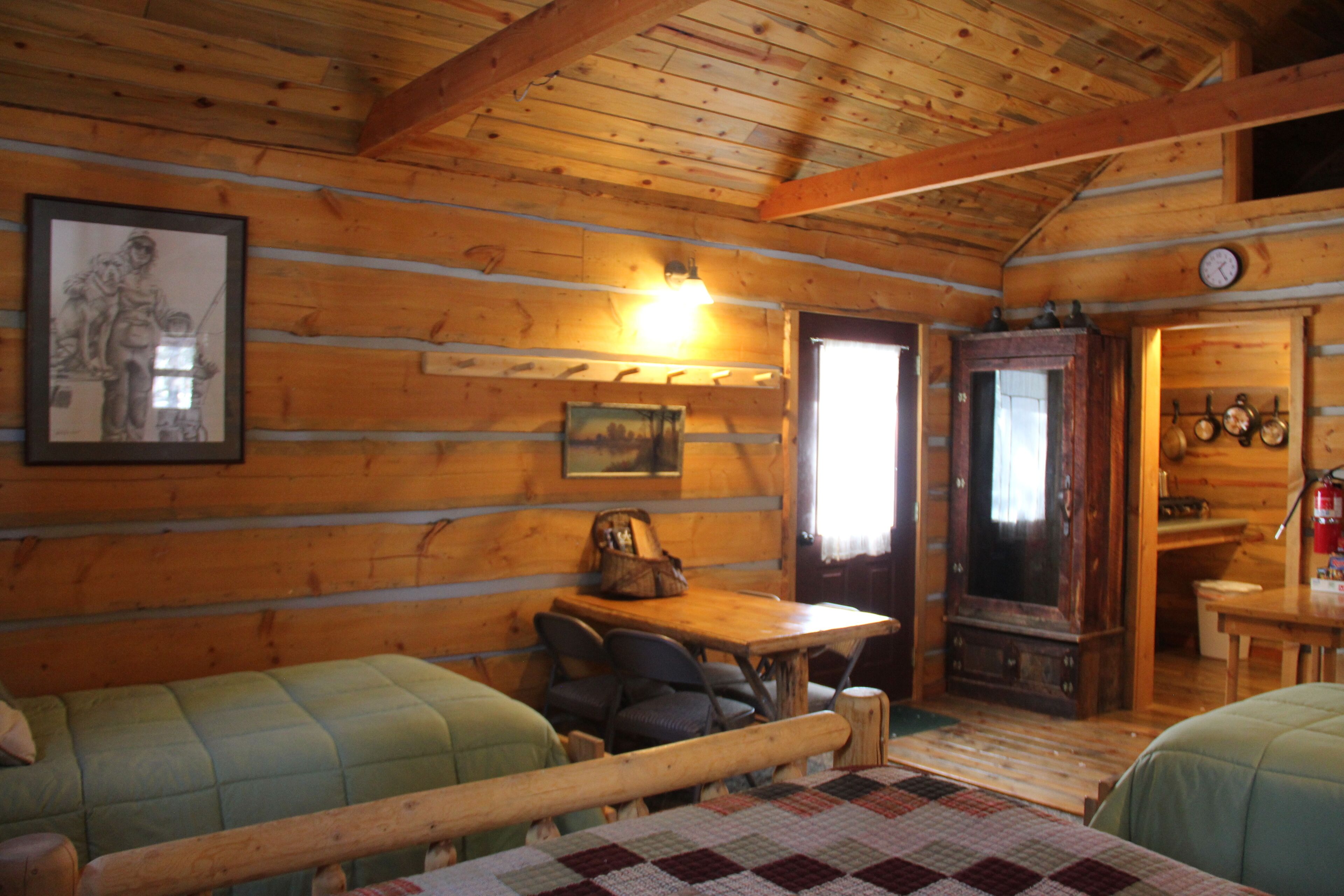 A cozy cabin interior with wooden walls, a dining area, and a sleeping area with two beds.