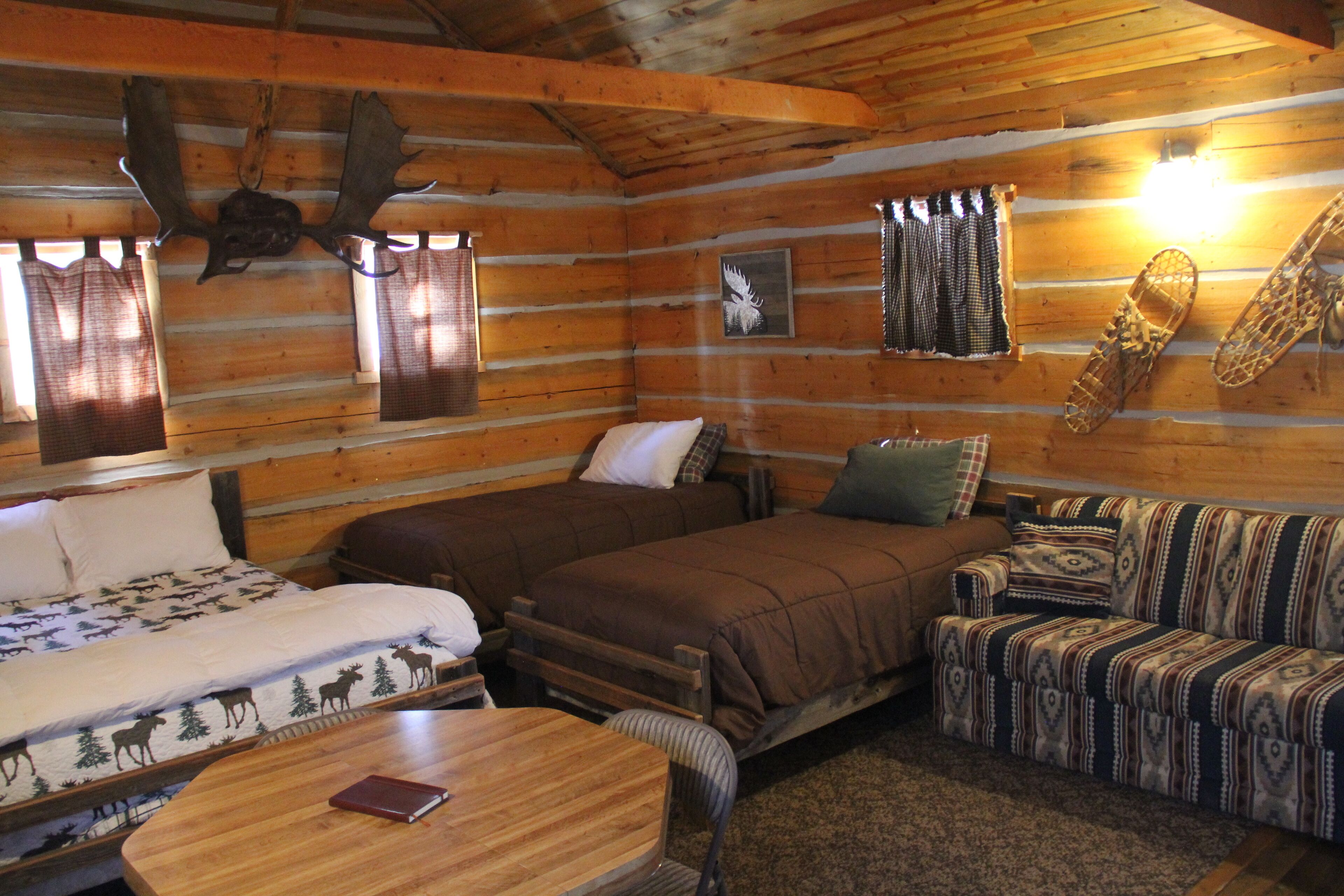 A log cabin interior with two beds, a sofa, and a wooden table.
