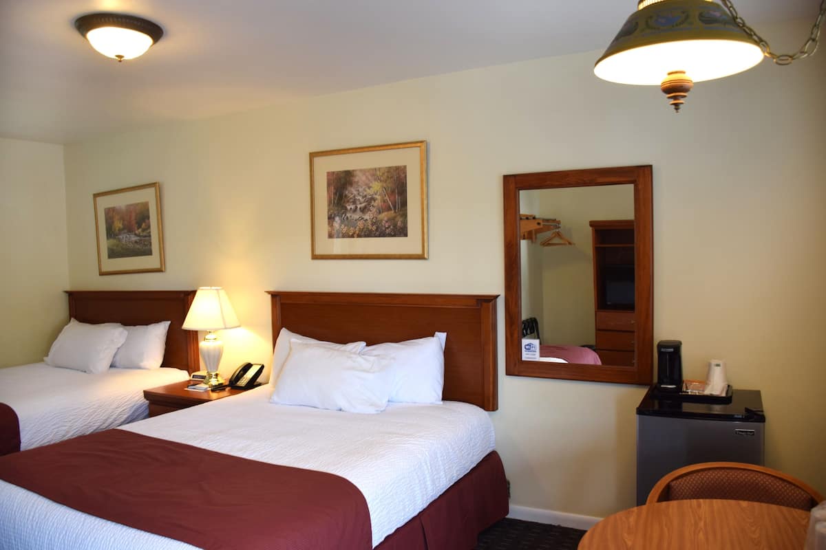 A hotel room with two beds, a desk with a lamp, a coffee maker, and a mirror on the wall.