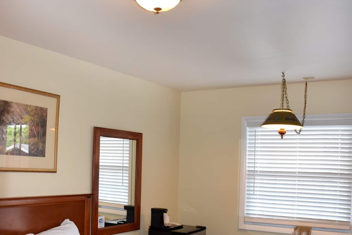 A hotel room with a large bed, a small table with chairs, a desk, a mirror, and a window with blinds.