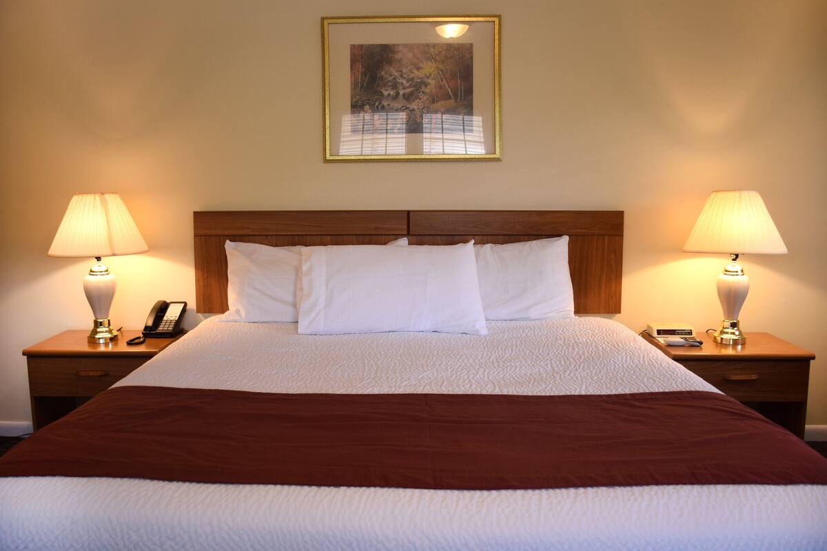 A neatly made bed with white linens and a brown accent, flanked by two bedside tables with lamps and a phone.