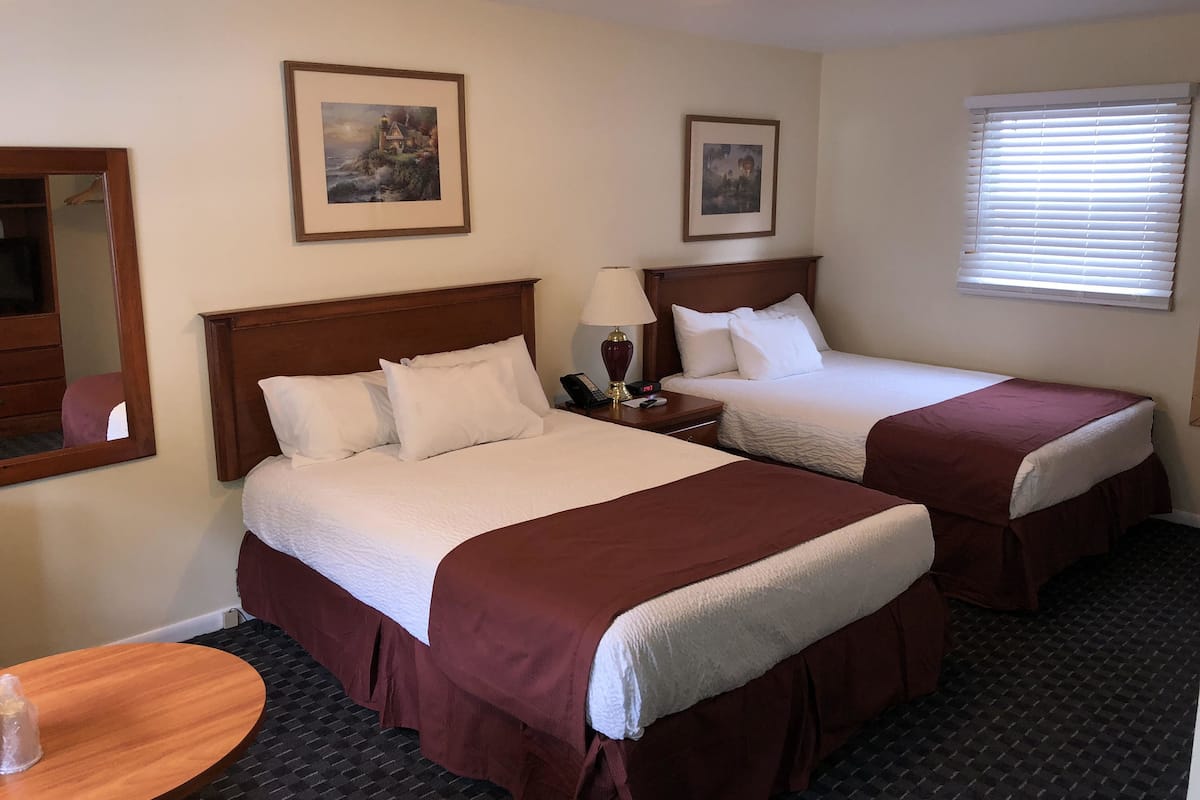 A hotel room with two beds, a round wooden table, and two framed pictures on the wall.