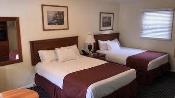 A hotel room with two beds, a round wooden table, and two framed pictures on the wall.