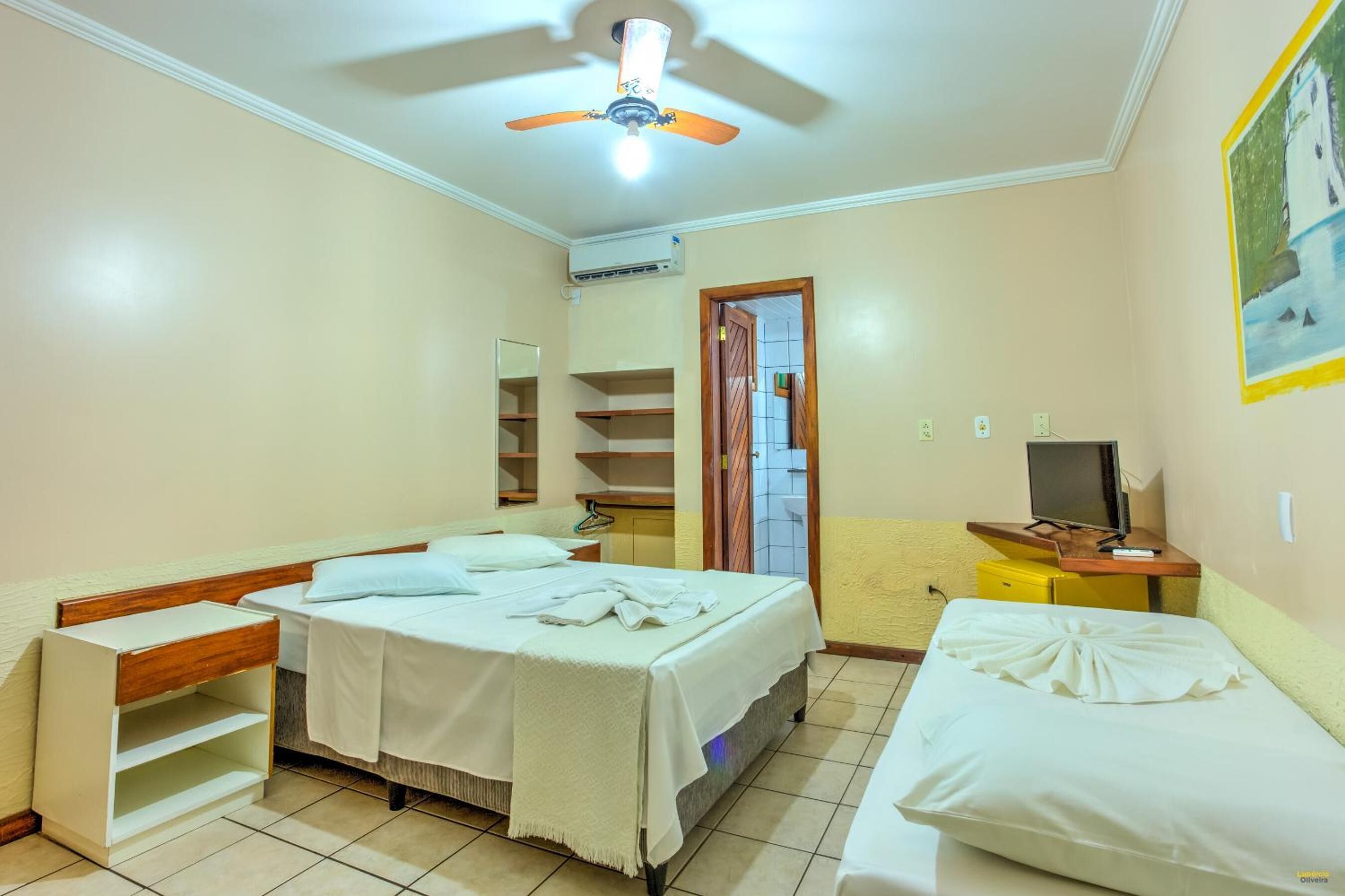 A hotel room with a bed, a desk with a chair, a television, a wardrobe, and a ceiling fan.