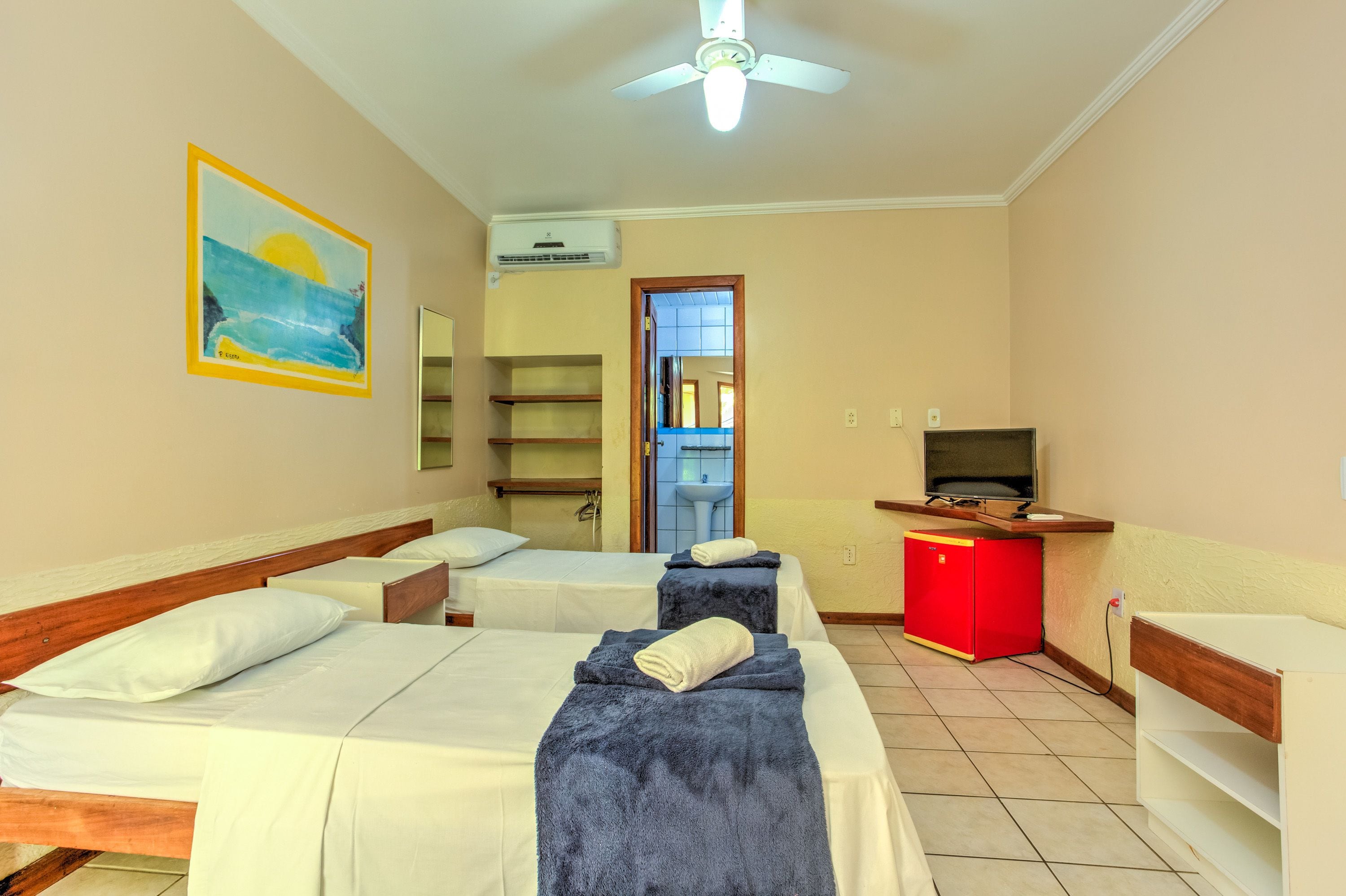 A hotel room with two beds, a TV, a red minibar, and a painting on the wall.