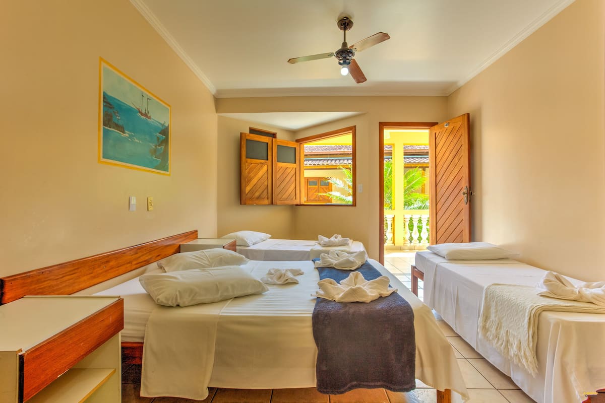 A hotel room with two beds, a ceiling fan, a painting, and a view of the outdoors.