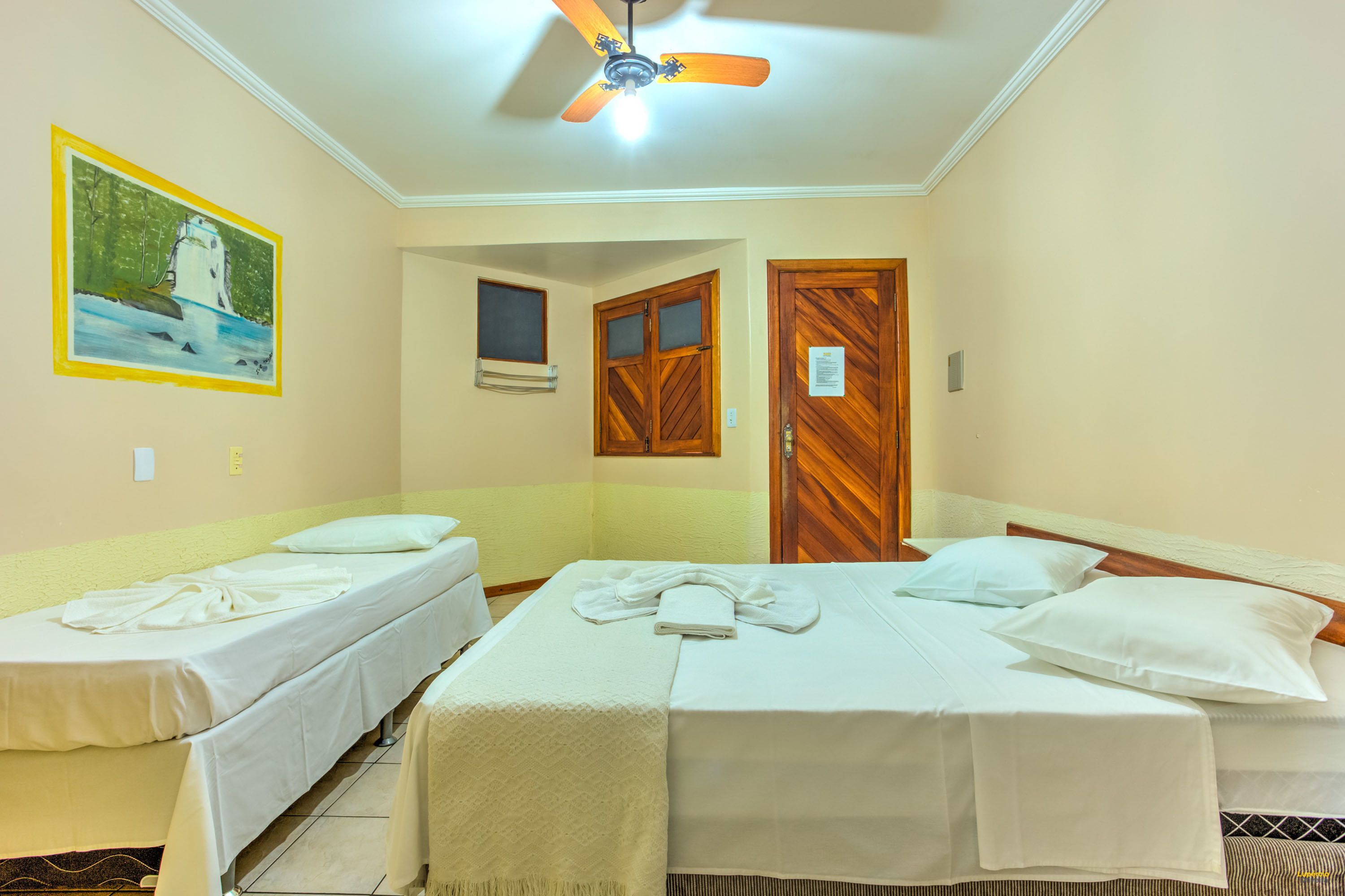 Habitación de hotel con dos camas individuales, un ventilador de techo, un cuadro en la pared y una puerta de madera.