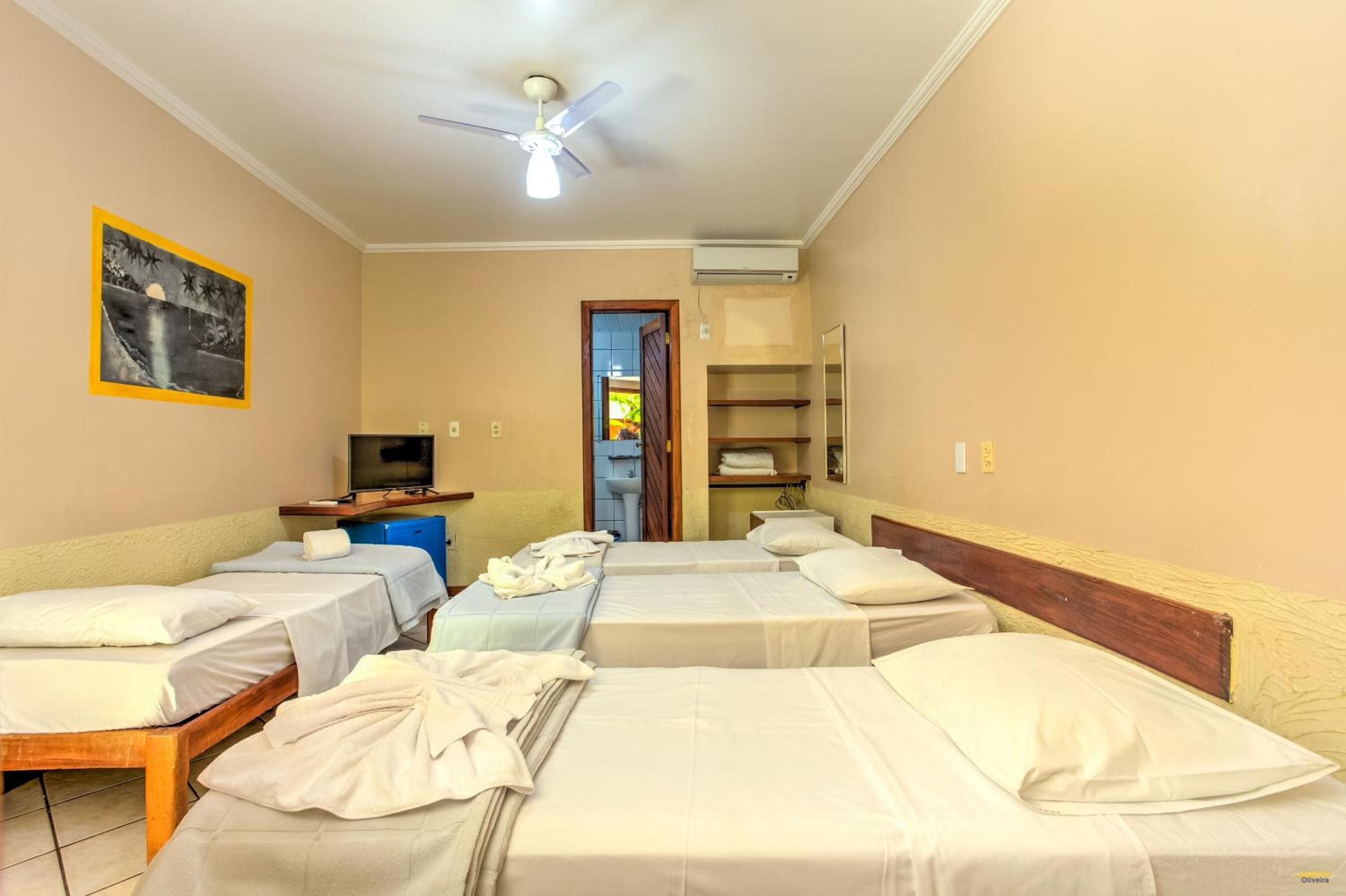 A hotel room with four single beds, a ceiling fan, a TV, and a bathroom visible through an open door.
