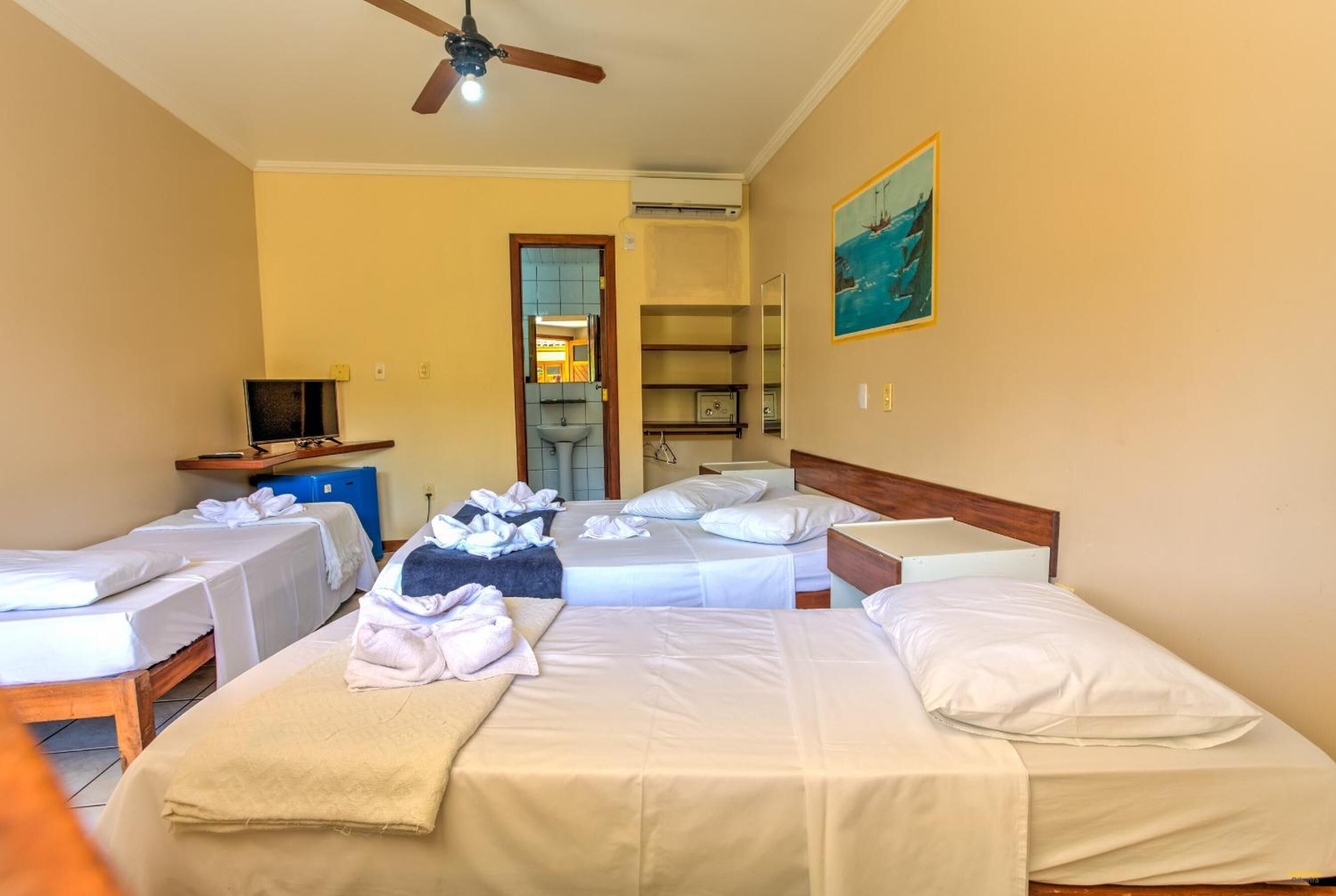 A hotel room with two single beds, a ceiling fan, a painting on the wall, and a desk with a computer.