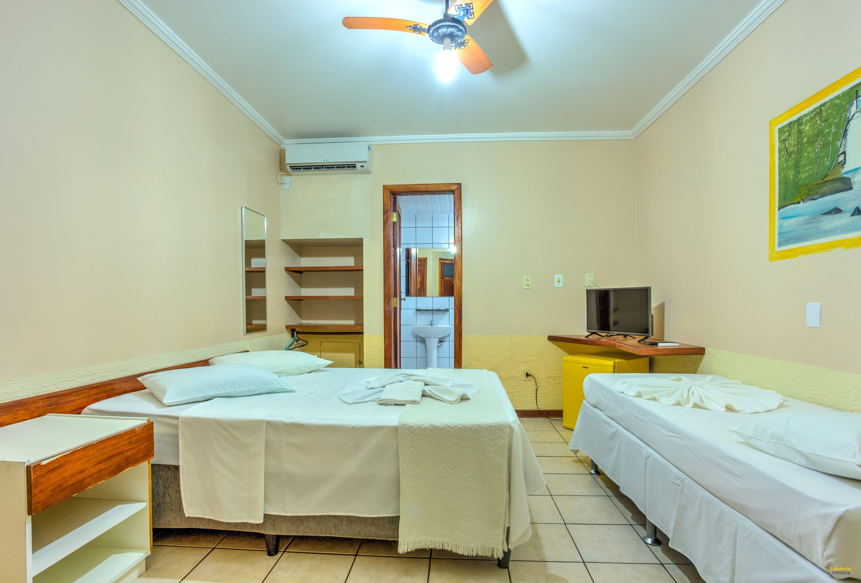 Habitación de hotel con dos camas, ventilador de techo, televisión y un cuadro en la pared.