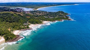 Vista aérea de una zona costera con playa, colinas boscosas y un pequeño poblado.