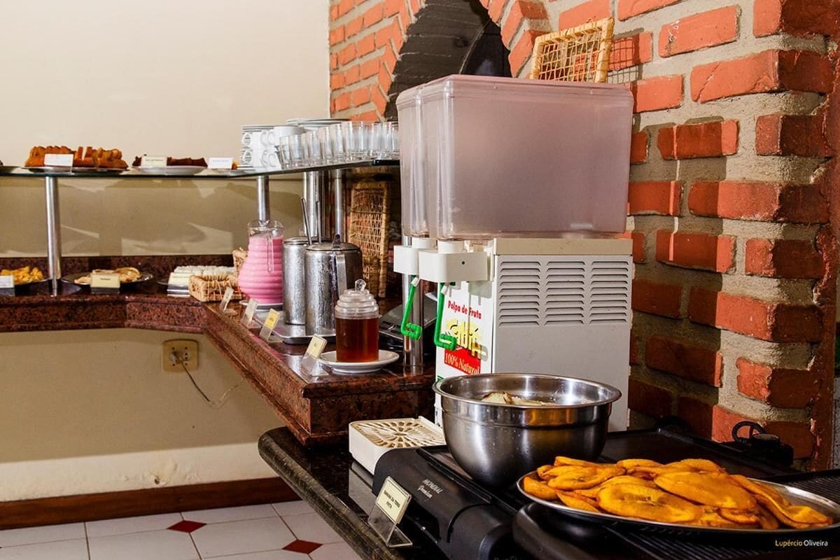 A buffet setup with various food items, a beverage dispenser, and a brick wall in the background.