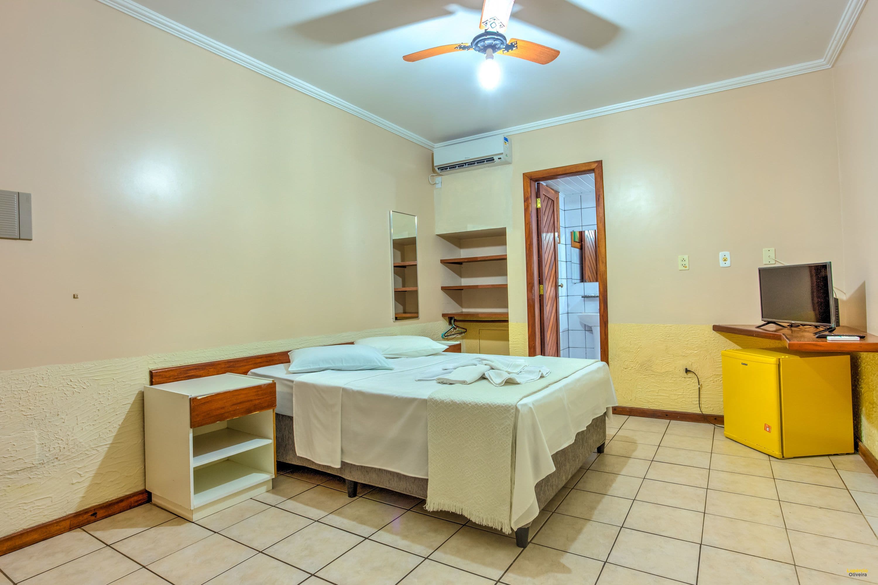 Un dormitorio con cama, mesita de noche, armario, ventilador de techo y televisor.
