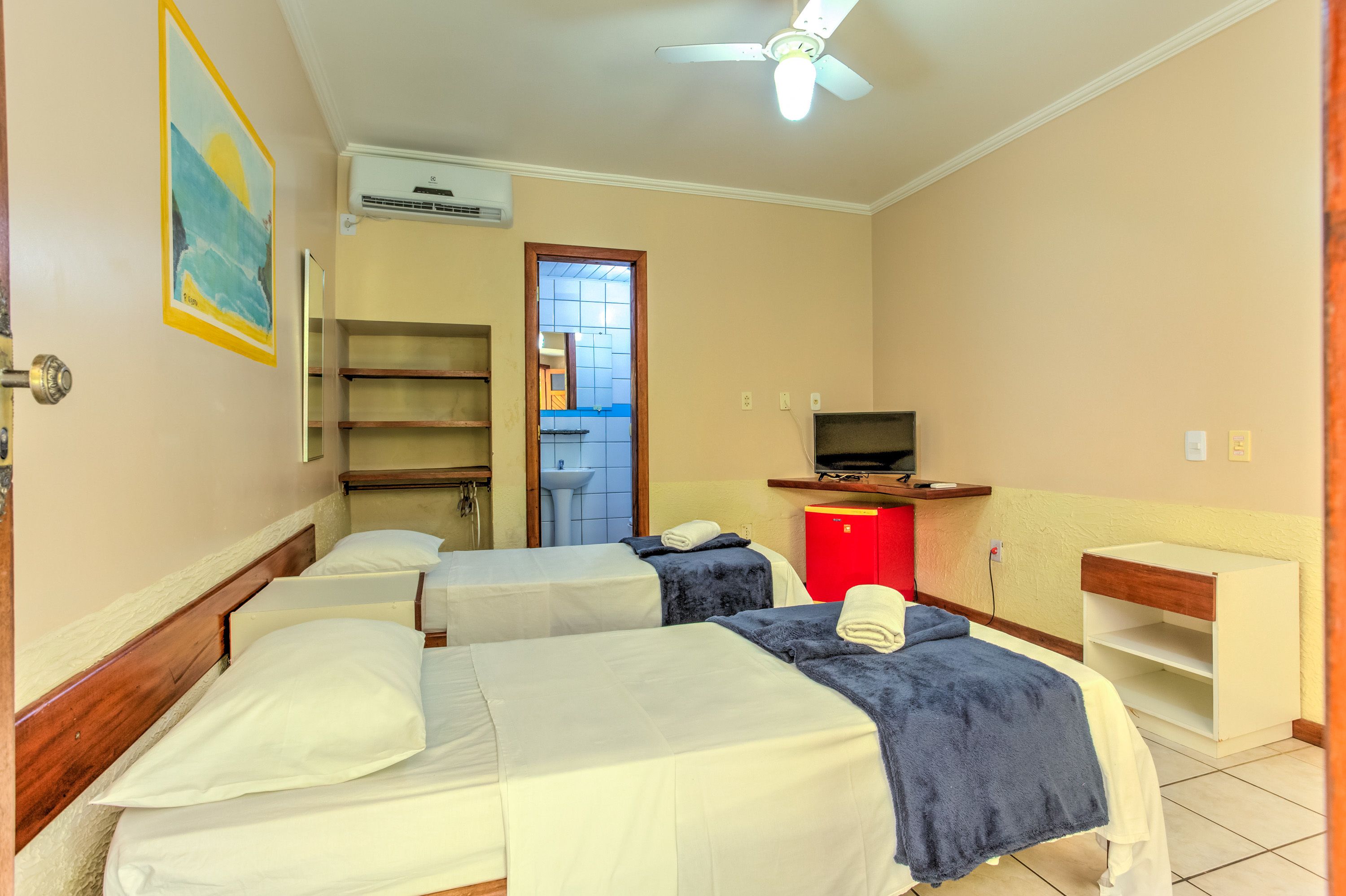 Une chambre d’hôtel avec deux lits, une télévision, une armoire rouge et un ventilateur de plafond.