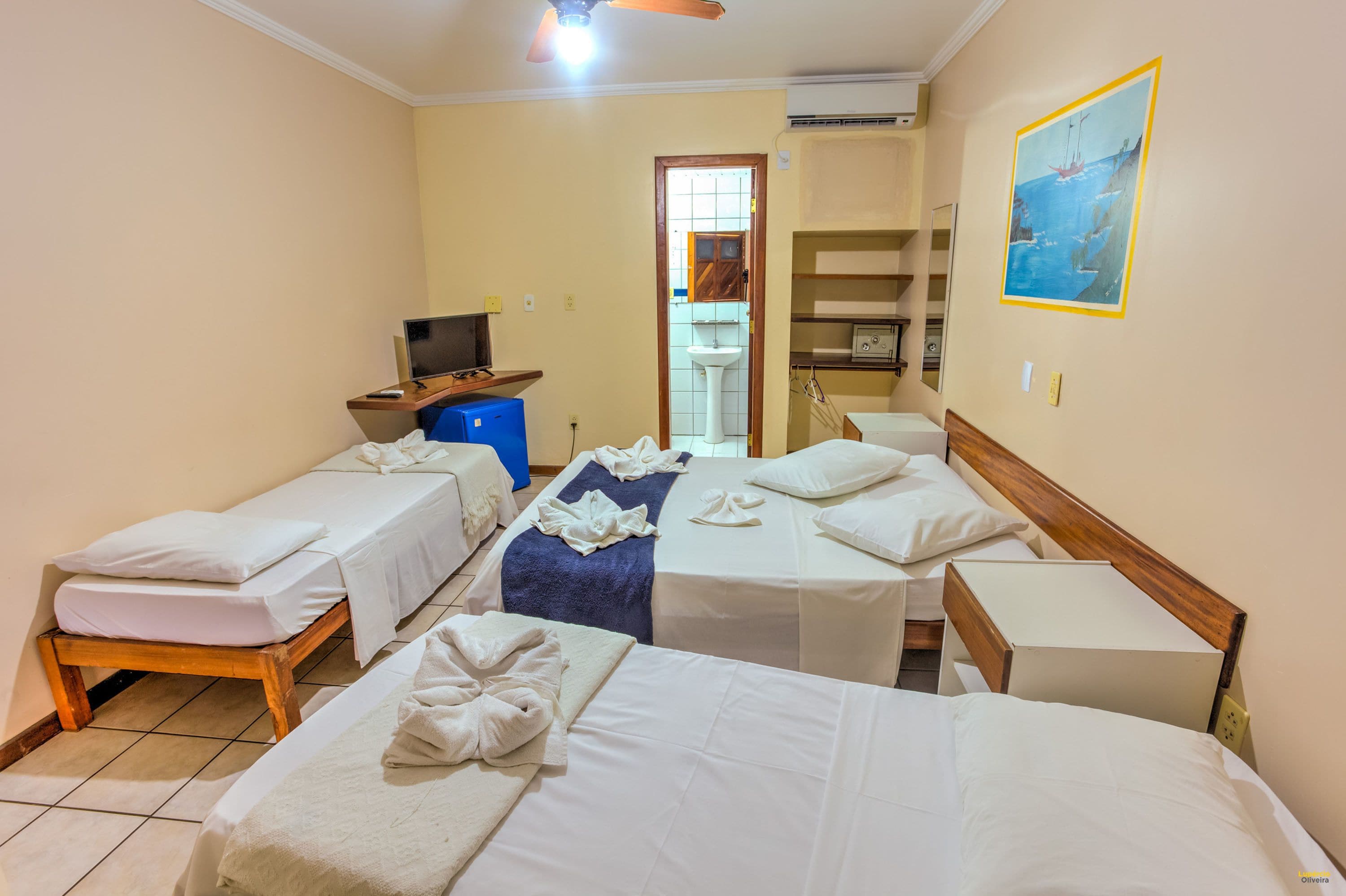Habitación de hotel con dos camas individuales, un escritorio con computadora, baño con lavamanos y espejo, y un cuadro en la pared.