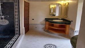 A bathroom with a black and white patterned floor, a wooden door, a sink with a mirror, and a decorative ceiling light.