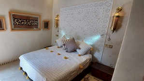 A bedroom with a bed, framed artwork, a decorative wall panel, and wall-mounted lights.