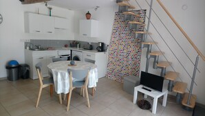 A compact kitchen with white cabinets, a dining table with chairs, a washing machine, and a colorful curtain. - Duplex apartment very well located and quiet (Bretenoux)